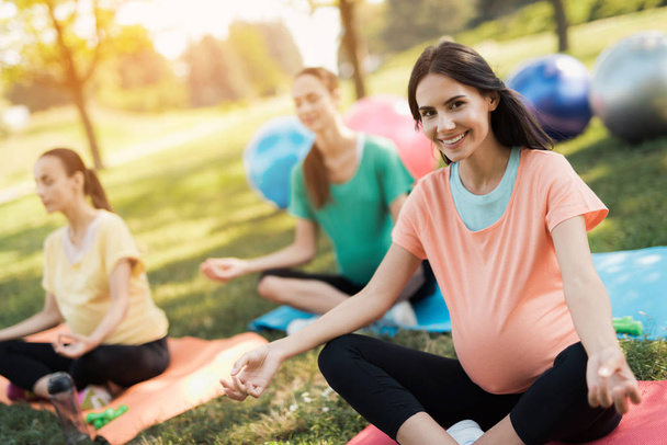 Pregnancy yoga. Three women sit on yoga mats in a lotus pose and smile - 写真・画像