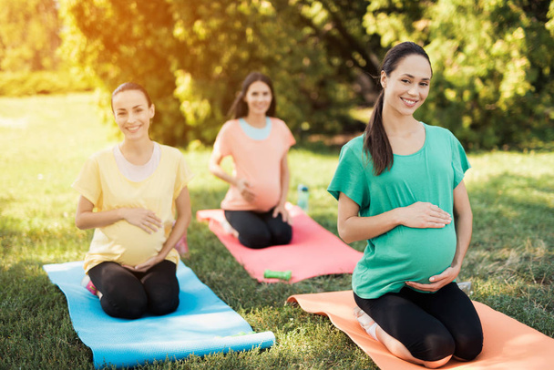 Pregnancy yoga. Three pregnant women doing yoga exercises in the park - Valokuva, kuva