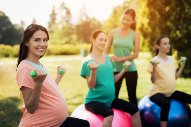 Pregnancy yoga. Three pregnant women are engaged in fitness in the park. They sit on balls for yoga - Photo, Image