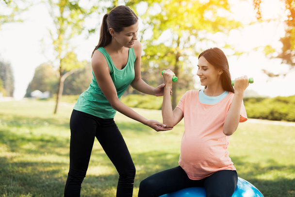 Pregnancy yoga. A coach helps a pregnant woman to do exercises on a ball for yoga - Valokuva, kuva