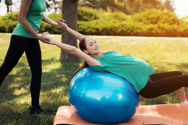 Pregnancy yoga. A woman is doing exercises on a blue ball for yoga. The coach helps her - 写真・画像