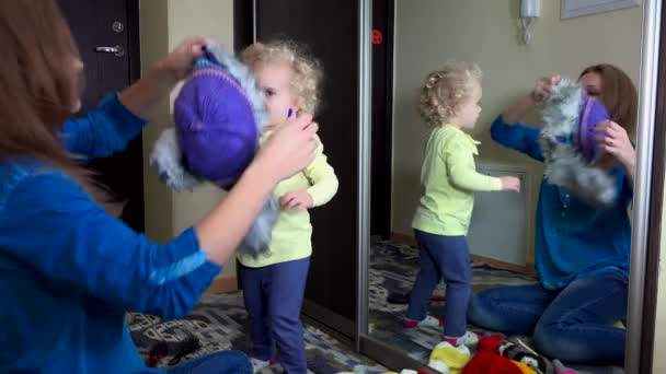 Heureuses filles familiales mesurant chapeaux d'hiver chauds près du miroir
 - Séquence, vidéo