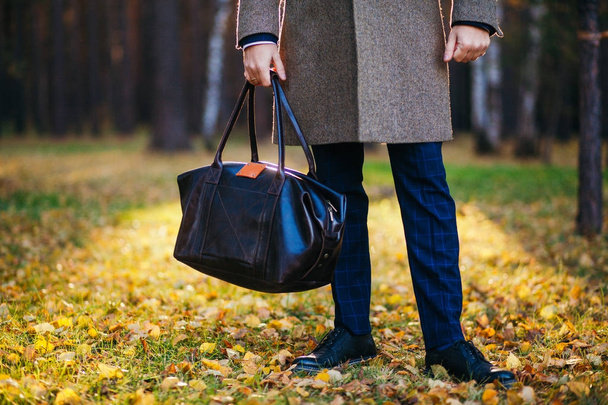 Clous up of the man in a coat and a leather bag in the beautiful autumn wood - Фото, изображение