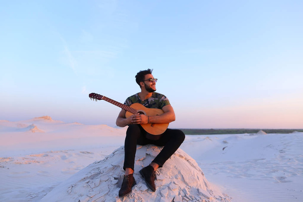 魅力的なアラビア人の丘の上に座って、ギターで歌を歌っています。 - 写真・画像