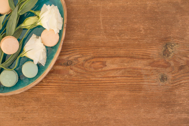 Aufnahme von weißer Lisianthus mit rosa und blassgrünen Makronen in grünem und braunem Keramikteller auf rustikalem Holztisch, mit Kopierraum - Foto, Bild