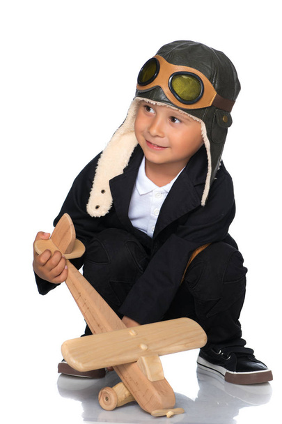 A little boy in a pilots cap and a wooden plane in his hand - Фото, зображення