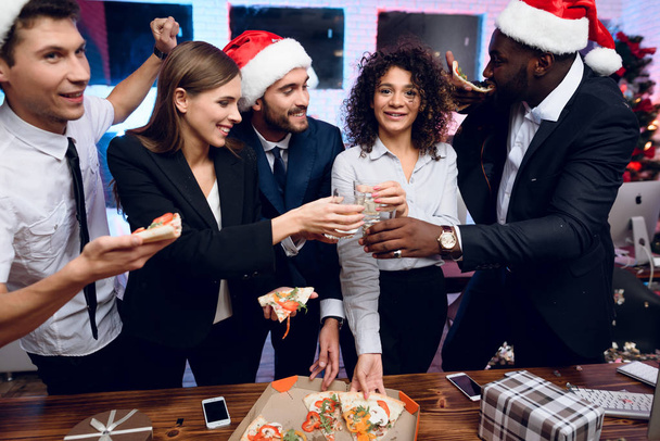 People are preparing to meet the new year in the office. They hold glasses with champagne and pizza. - Foto, imagen