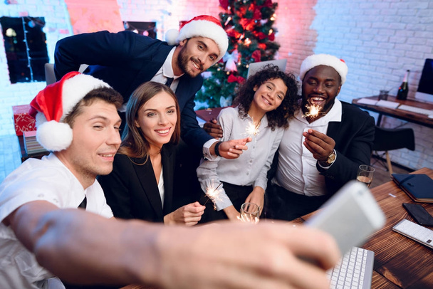 People are preparing to meet the new year in the office. They sit with champagne glasses in their hands and make selfies - Фото, изображение