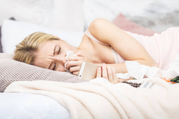 Больная красивая женщина лежит в постели с высокой температурой. Холод, грипп, лихорадка и мигрень с термометром и телефоном. В стрессе. Крупный план
. - Фото, изображение