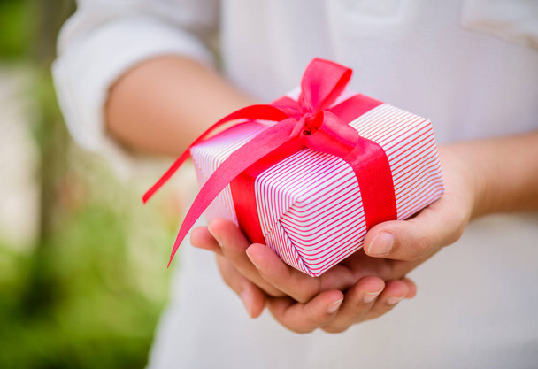 Γυναικείο χέρι κρατά ένα κουτί δώρου με κόκκινη κορδέλα.  - Φωτογραφία, εικόνα