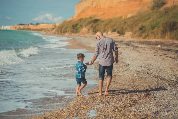 Dream touch scene of handsome father walking on sea side stone beach with cute son wearing stylish clothes enjoy summer time together - Foto, afbeelding