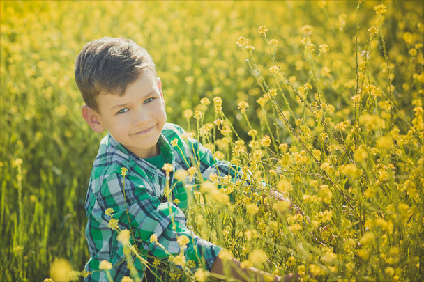 Handsome happy boy child enjoy posing summer time vacation on field yellow flowers wearing rustic village style clothes.Cute kid dreaming about future life - Photo, Image