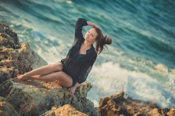 Hot sexy stylish dressed young lady brunette hairs and pinky cheeks with open legs shoulders and arms posing sensuality on sea side rocky beach. seductive woman awaiting her future seaman husband - Φωτογραφία, εικόνα