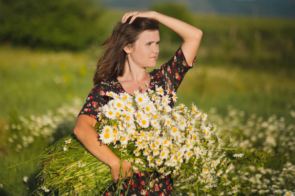 Charming adorable young lady woman dark brunette hairs and green eyes tender sexy posing with flowers wreath on head top and huge bouquet of wild daisy chamomile wearing stylish dress. - Photo, Image
