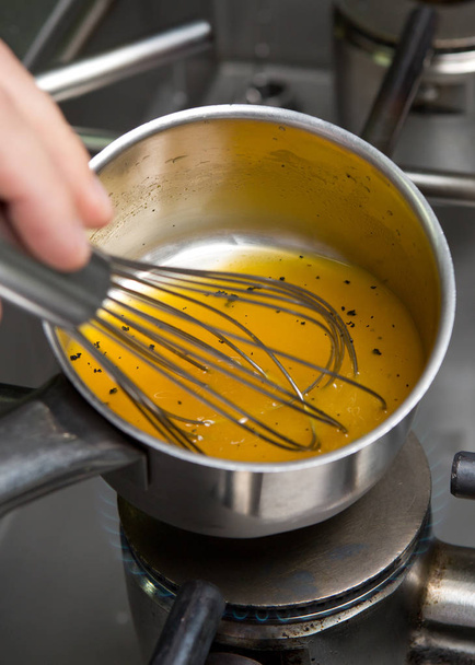 A metal mixing bowl full of fresh chicken stock being reduced over a flaming hob.The chicken stock is being whisked  - Valokuva, kuva