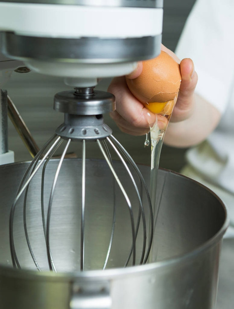 A fresh free range egg being cracked into an industrial metal whisking machine. Shot with a shallow depth of field. - 写真・画像