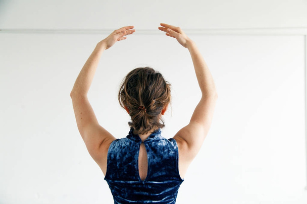 若い女性パフォーマーは、ブルー ベルベット ドレス白広々 としたロフトのコンテンポ ラリー ダンスの要素を練習に身を包んだ。後ろからを表示します。自然な照明。コピー領域と水平方向で構成. - 写真・画像