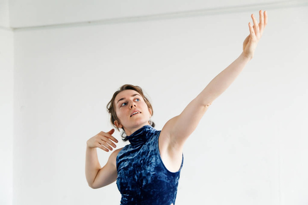 Young female performer dressed in blue velvet dress practicing contemporary dance elements in white spacious loft. Natural lighting. Horizontal composition with copy space. - Φωτογραφία, εικόνα
