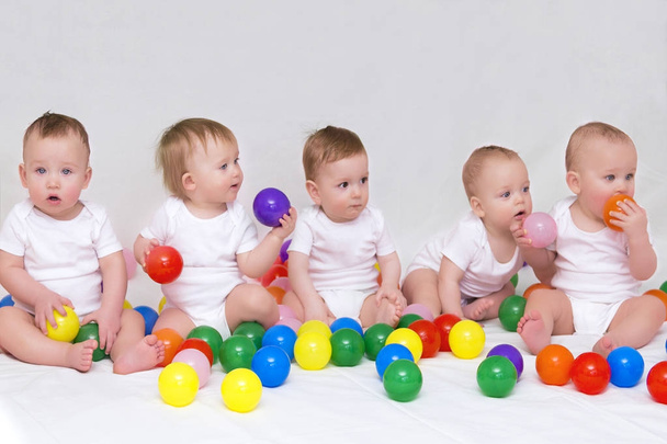 Retrato de cinco bebês bonitos no fundo de luz jogando com bolas coloridas
 - Foto, Imagem