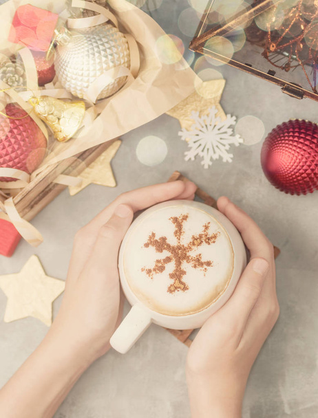 Top view flat lay hands holding White mug of cappuccino with cinnamon powder snowflake among christmas toys - Photo, image