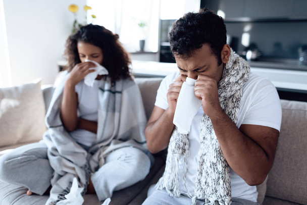 Black man and woman are sitting on the couch. They catch a cold and blow their nose in paper napkins. - Photo, Image