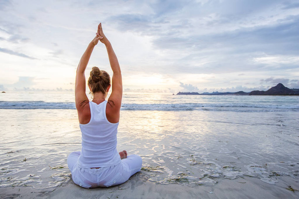 Caucasian woman practicing yoga at seashore of tropic ocean - Valokuva, kuva