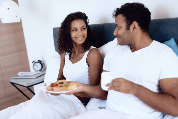 Μαύρος άνδρας και γυναίκα στην κρεβατοκάμαρα. Έχουν πρωινό στο κρεβάτι. - Φωτογραφία, εικόνα