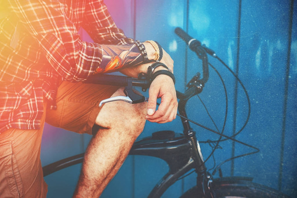 Unrecognizable Man Sitting On A Bicycle Near Blue Wall And Ligth Background Daily Lifestyle Urban Resting Concept Toned And Scratches - Foto, Imagem