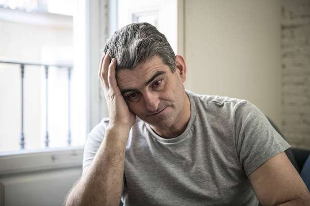 trauriger und besorgter Mann mit grauen Haaren auf der heimischen Couch sitzend und schauend - Foto, Bild