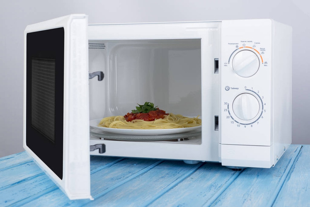 Un nuovo forno a microonde bianco, su una superficie di legno blu per il riscaldamento
 - Foto, immagini