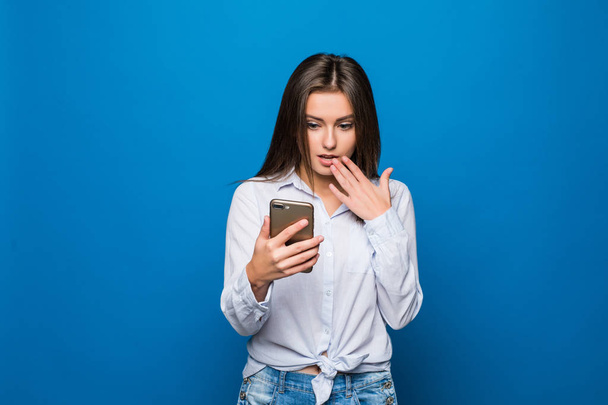Woman feeling shock reading on mobile phone on blue background - Photo, Image