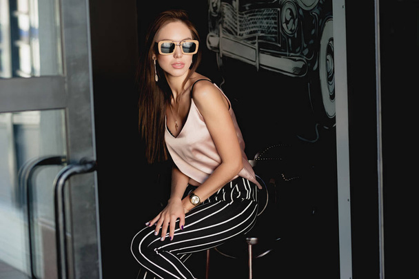 Young and beautiful girl in a beige t-shirt and black breeches in a white stripe. Womens fashion. Urban way of life - Photo, Image