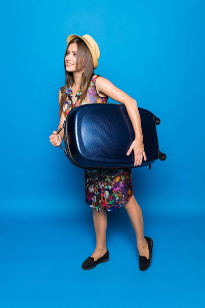 Щаслива молода жінка, що тримає валізу, піднімає ногу як бігун. Час для літніх канікул на синьому фоні
. - Фото, зображення