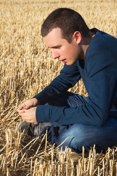 Promyšlené mladé profil sedí na pokosené obilné pole - Fotografie, Obrázek