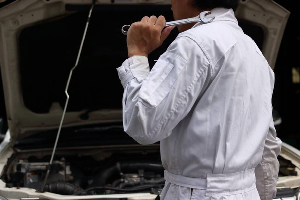 Boční pohled na profesionální mechanik mladíka v jednotné hospodářství klíč proti auto v otevřené kapuce na opravu garáže. - Fotografie, Obrázek