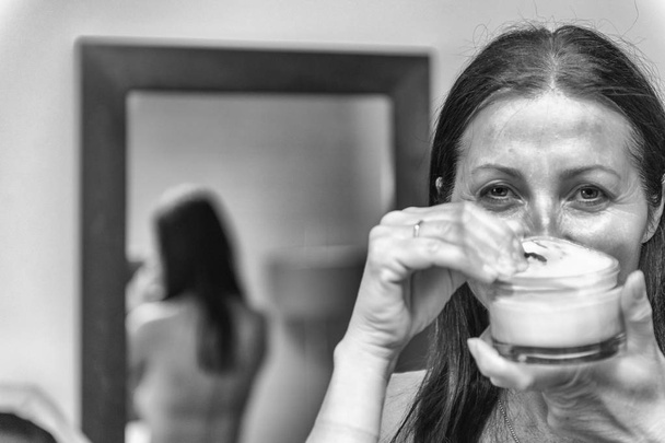 Mulher de 40 anos preparando hidratante em seu rosto. Álcool menina sorridente
 - Foto, Imagem