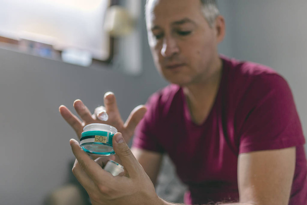 Mature man applying cosmetic product. Handsome middle aged man holding container with cream - Φωτογραφία, εικόνα