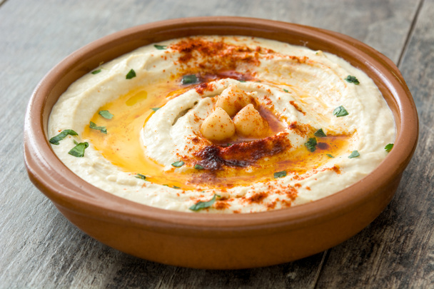 Chickpea hummus in bowl on wooden table. - Фото, изображение