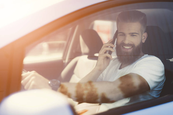 A young man with a beard sits at the wheel of an electric vehicle. - 写真・画像