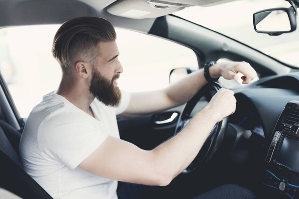 A young man with a beard sits at the wheel of an electric vehicle. - Zdjęcie, obraz