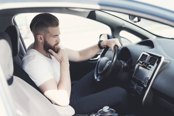 A young man with a beard sits at the wheel of an electric vehicle. - Foto, Bild