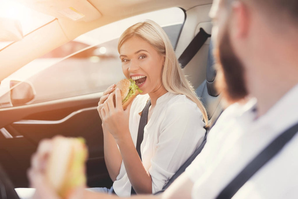 A srác és a lány enni hamburgert, ül a szalonban, az elektromos autó. - Fotó, kép