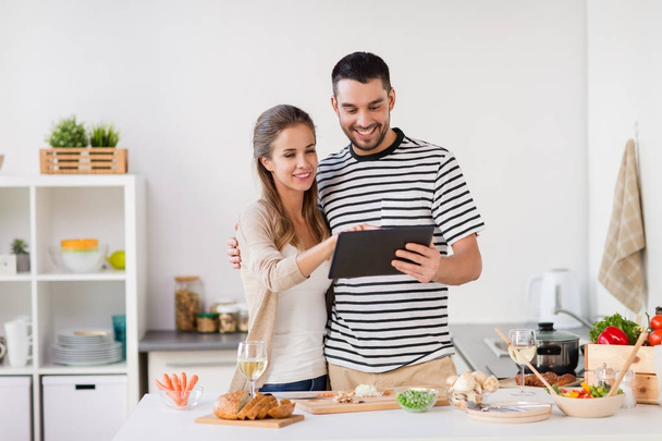 happy couple with tablet pc cooking food at home - Foto, Bild