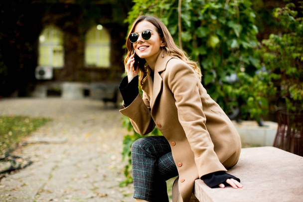 Jeune femme assise en plein air et utilisant un téléphone mobile
 - Photo, image