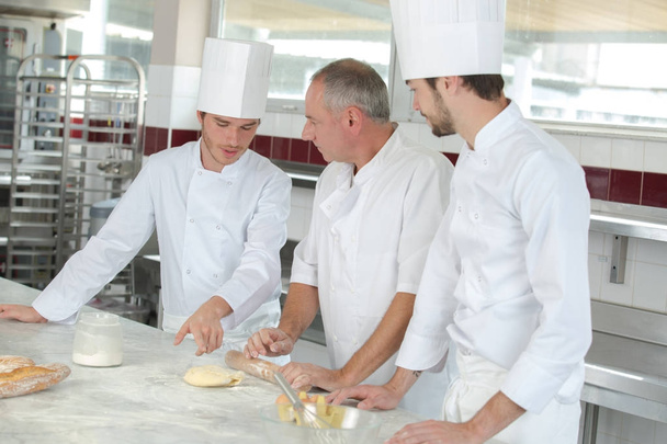 male baker showing his apprentices the secrets of pastry - 写真・画像