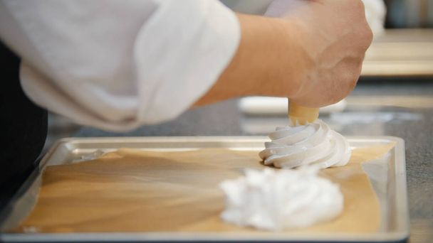 Cocinar Pavlova merengue postre tubo de pastelería difundir merengue en una bandeja para hornear
 - Foto, imagen