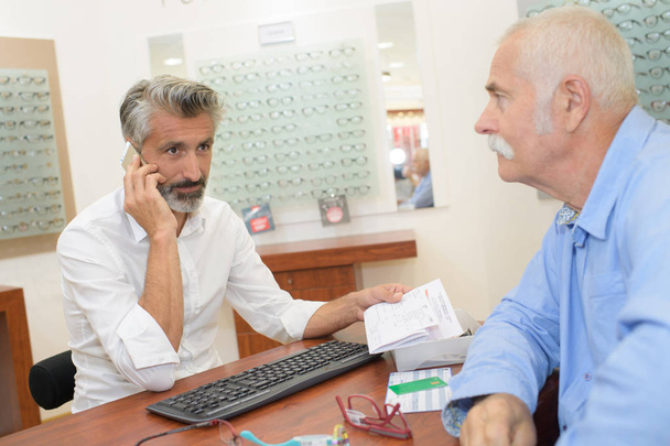 optician helping senior male patient with new eyeglasses - Foto, Imagem
