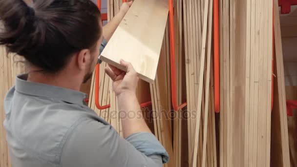 Young man selecting wood boards in a hardware store or warehouse - Séquence, vidéo