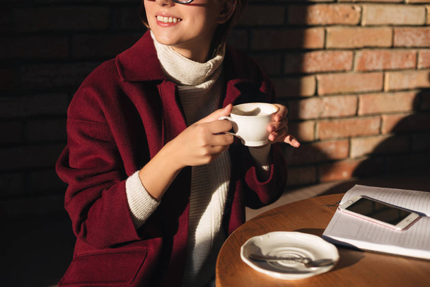 Close-up foto van vrouw lichaam zitten en houden van kopje koffie aan de tafel van café op straat - Foto, afbeelding
