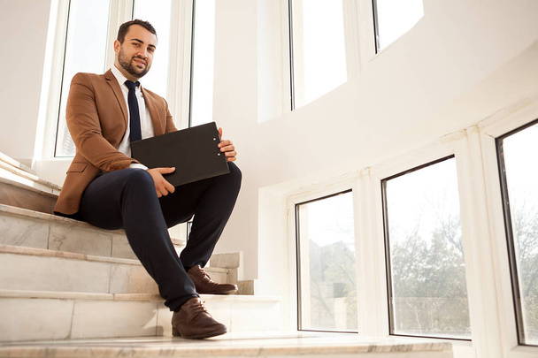 Un exitoso hombre de negocios sentado en las escaleras con una carpeta en las manos
 - Foto, Imagen